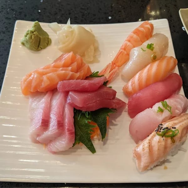 A white rectangular plate filled with various sushi and sashimi, including salmon, tuna, shrimp, and white fish.