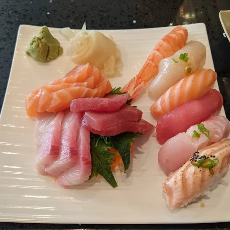 A white rectangular plate filled with various sushi and sashimi, including salmon, tuna, shrimp, and white fish.