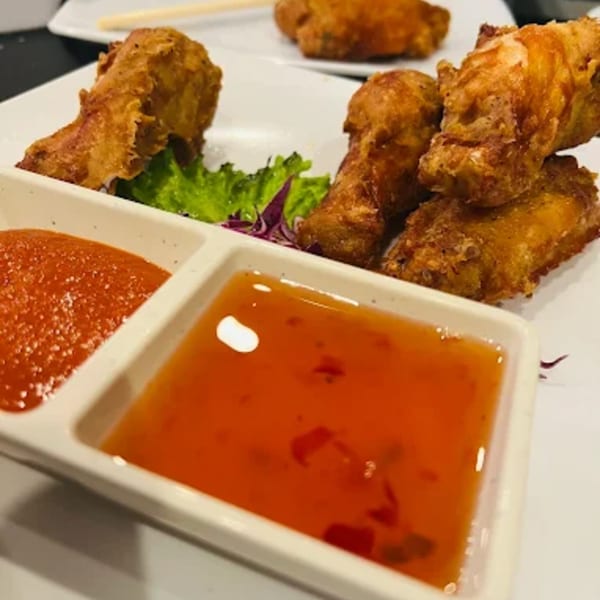 Crispy fried chicken wings with two dipping sauces, one red and one orange, on a white plate.