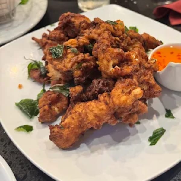 Crispy fried calamari with green herbs and a side of sweet chili dipping sauce on a white plate.