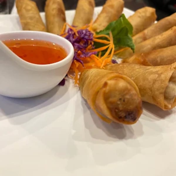 Crispy golden spring rolls with sweet chili dipping sauce, garnished with shredded carrots and purple cabbage.