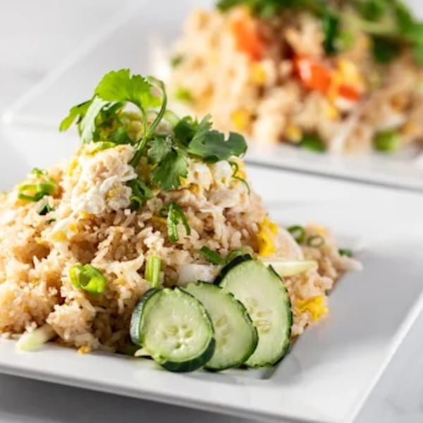 Two plates of Zato Thai Cuisine's fried rice with egg, green onions, cilantro, and cucumber slices.