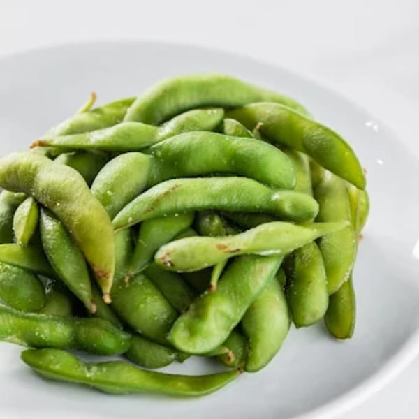 Close-up of a pile of vibrant green edamame pods, lightly salted, on a white plate.