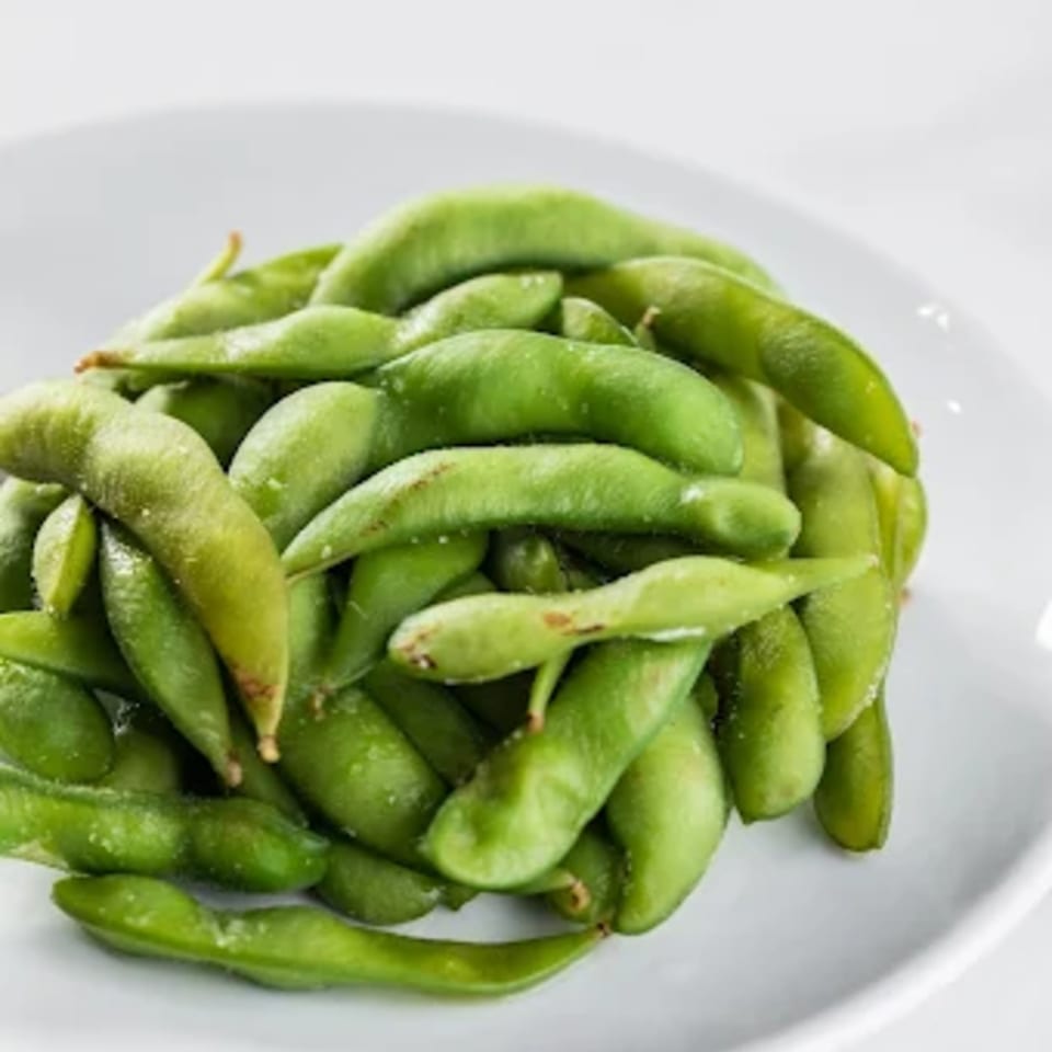 Close-up of a pile of vibrant green edamame pods, lightly salted, on a white plate.