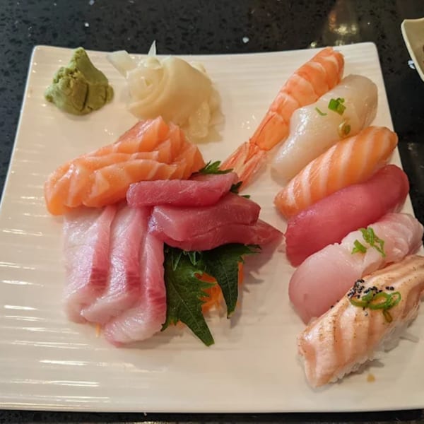 A white rectangular plate filled with various colorful sushi and sashimi pieces, with wasabi and ginger.